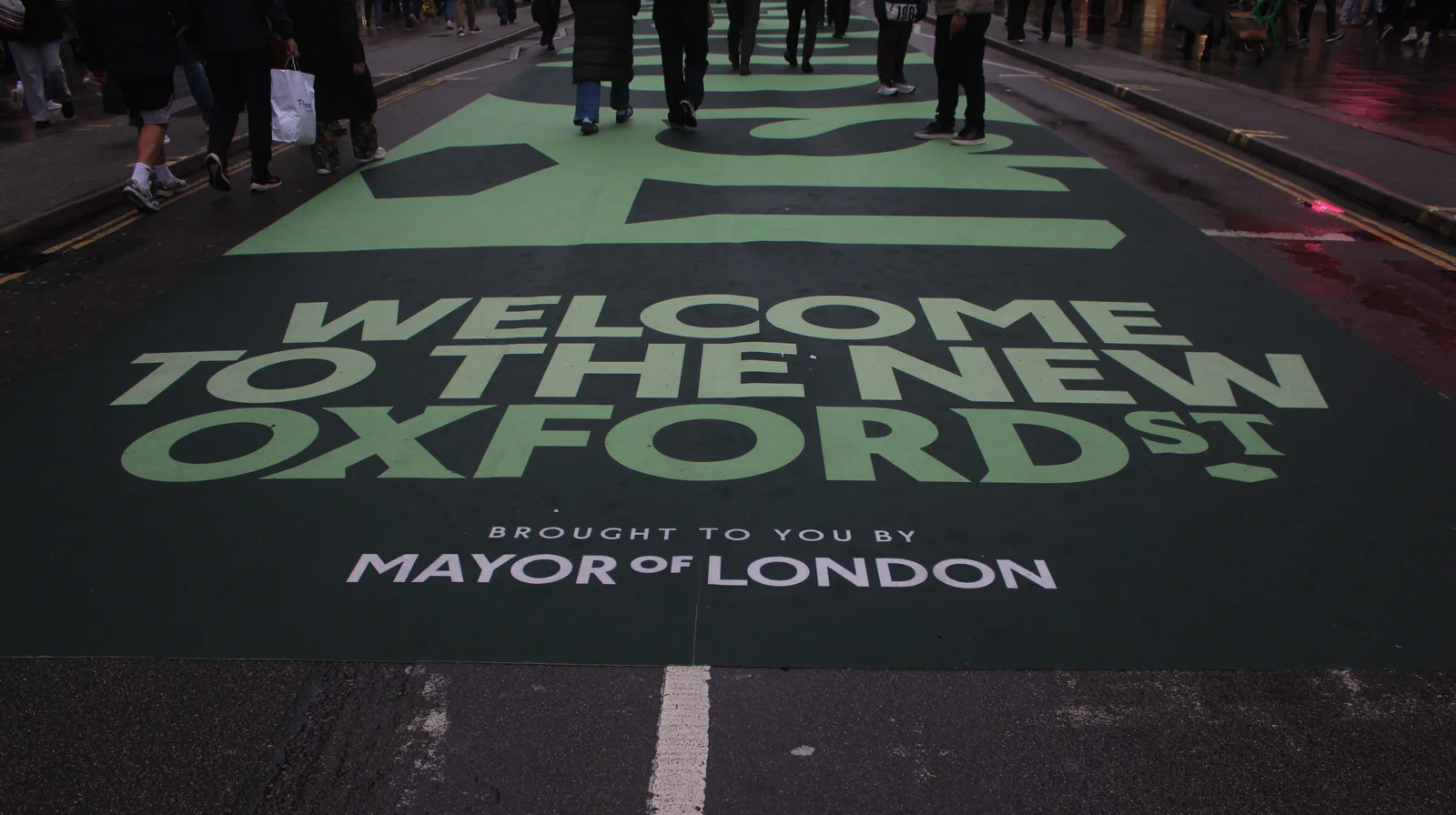 Green Welcome to the new Oxford St marking painted across the road as pedestrians walk over it on opening day
